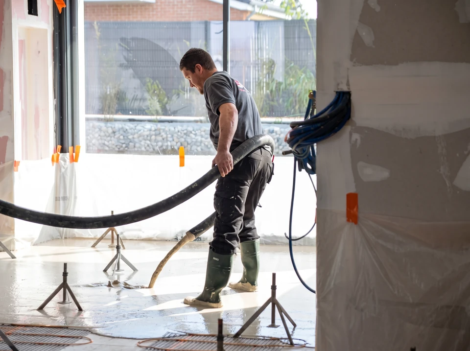 Ouvrier en bottes en caoutchouc manipule un tuyau de pompage flexible sur un chantier intérieur en cours de finition
