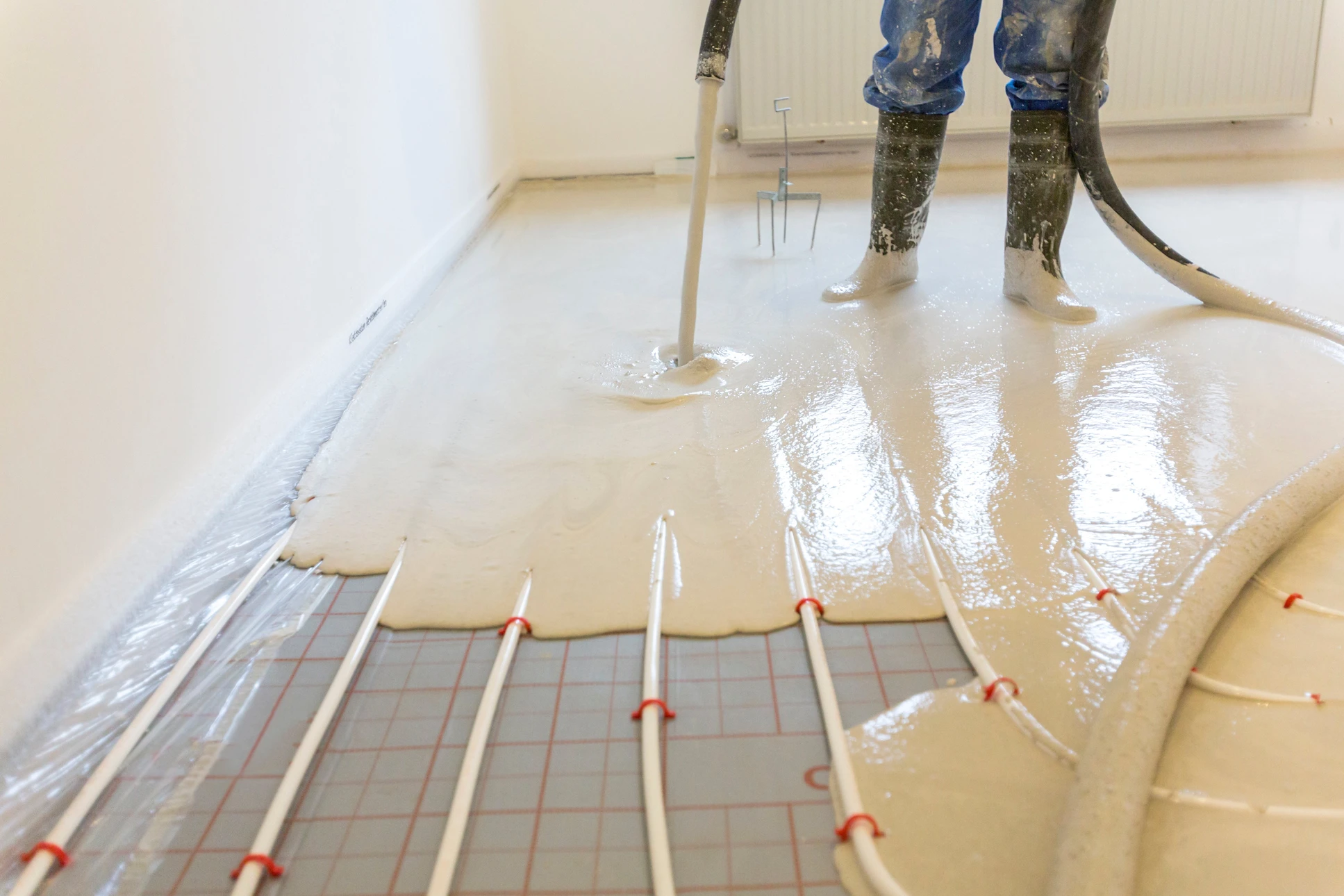 Ouvrier en combinaison appliquant une chape liquide autolissante sur plancher chauffant