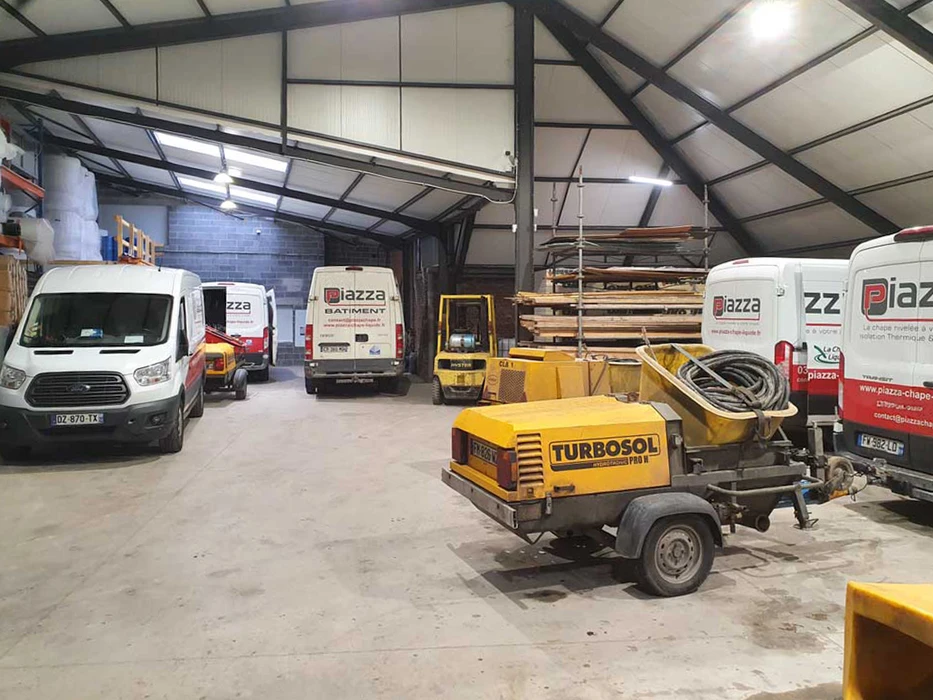 Entrepôt industriel intérieur abritant plusieurs véhicules utilitaires Ford Transit blancs marqués **Piazza Bâtiment**, spécialisés en chape liquide